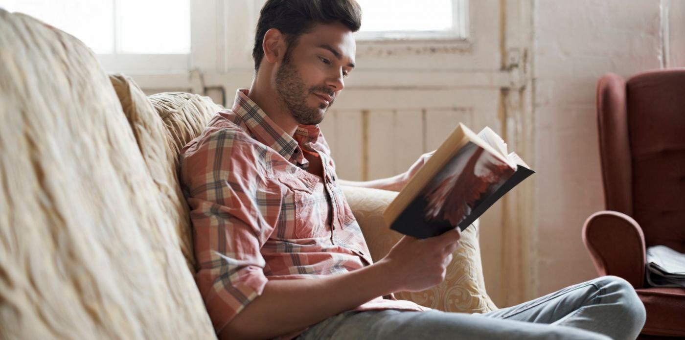Un ragazzo seduto su un divano legge un libro e sorride