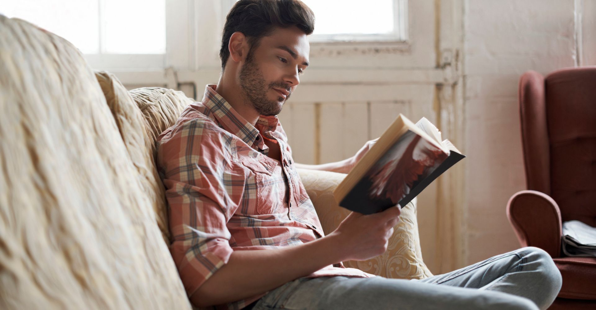 Un ragazzo seduto su un divano legge un libro e sorride