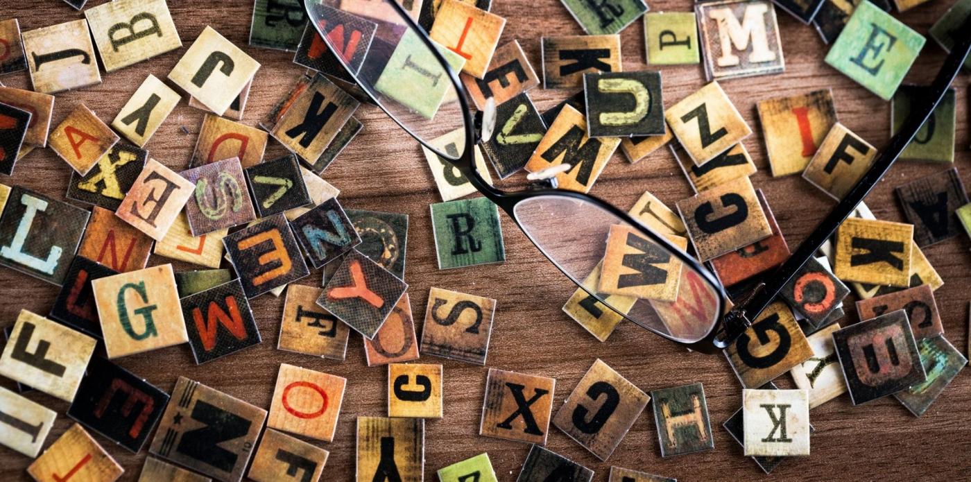 Un tavolo con un paio di occhiali poggiati su lettere intagliate nel legno