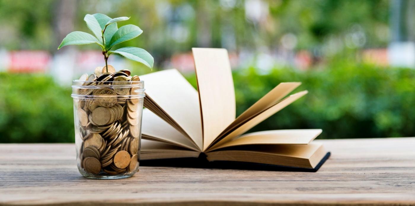 Un salvadanaio pieno di monete e un libro poggiati su un tavolo all'aperto