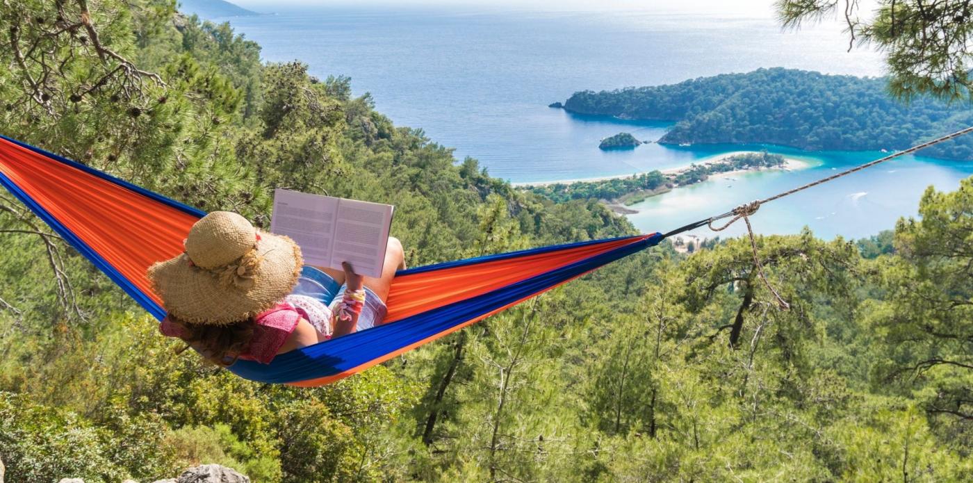 Donna su un'amaca che legge un libro in montagna con vista sul mare