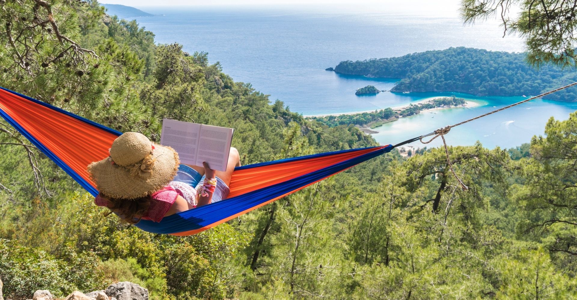 Donna su un'amaca che legge un libro in montagna con vista sul mare