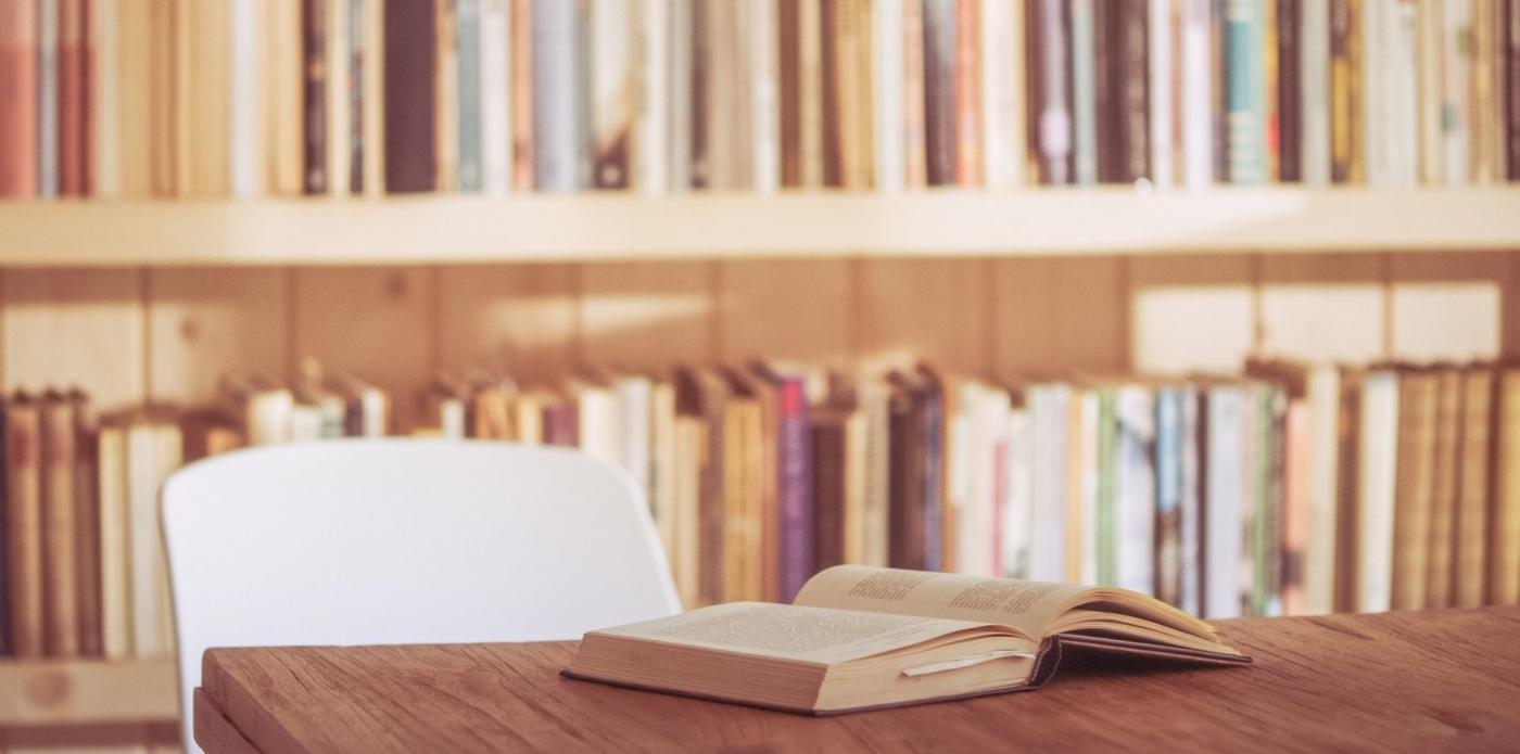 Un libro aperto su un tavolo, con dietro una libreria piena di libri