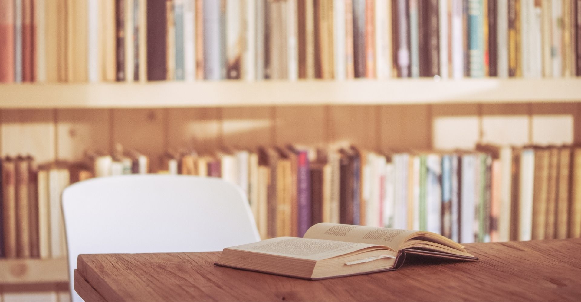 Un libro aperto su un tavolo, con dietro una libreria piena di libri