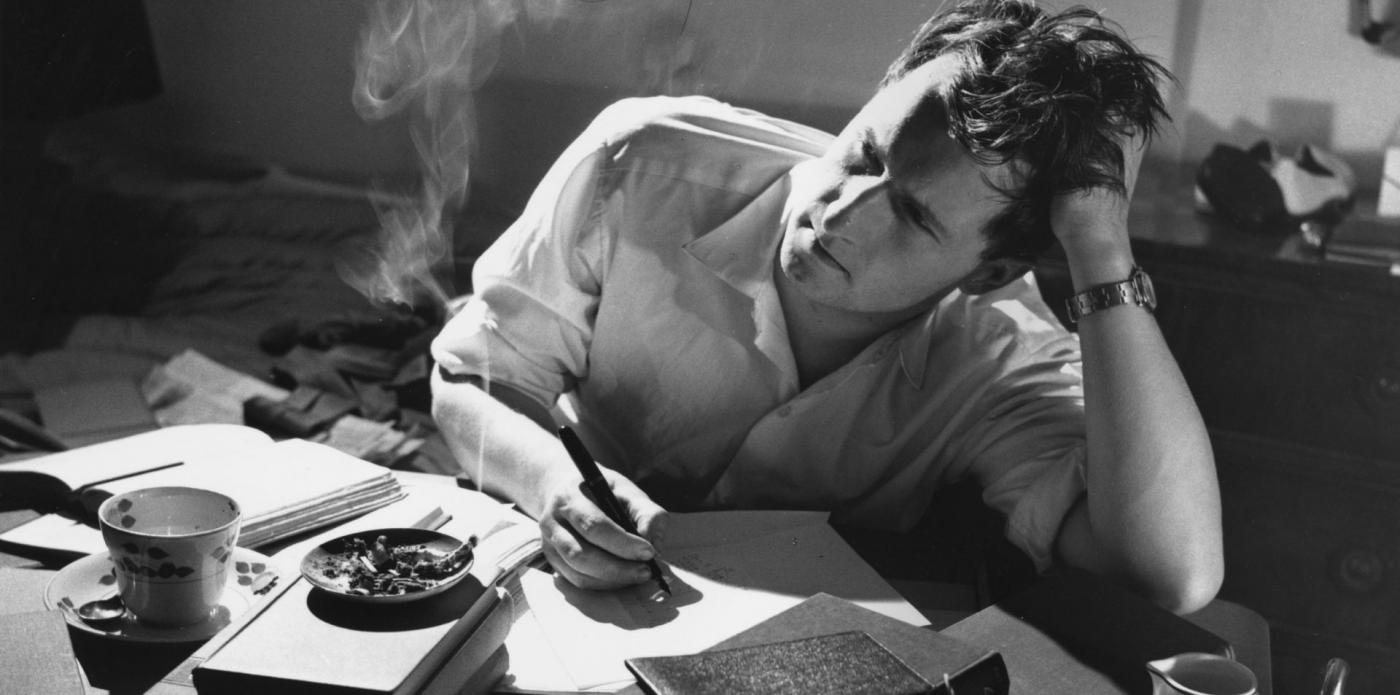 Un uomo seduto a una scrivania scrive su un foglio e riflette