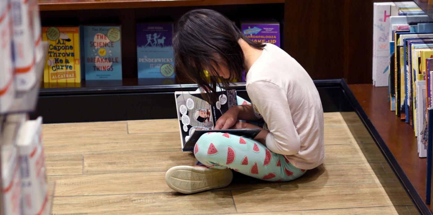 Una bambina legge un libro seduta per terra in una libreria