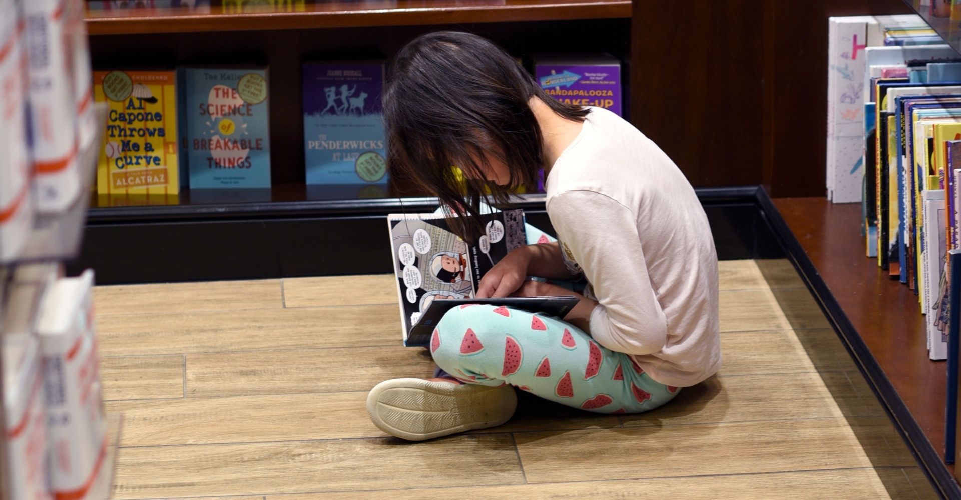 Una bambina legge un libro seduta per terra in una libreria