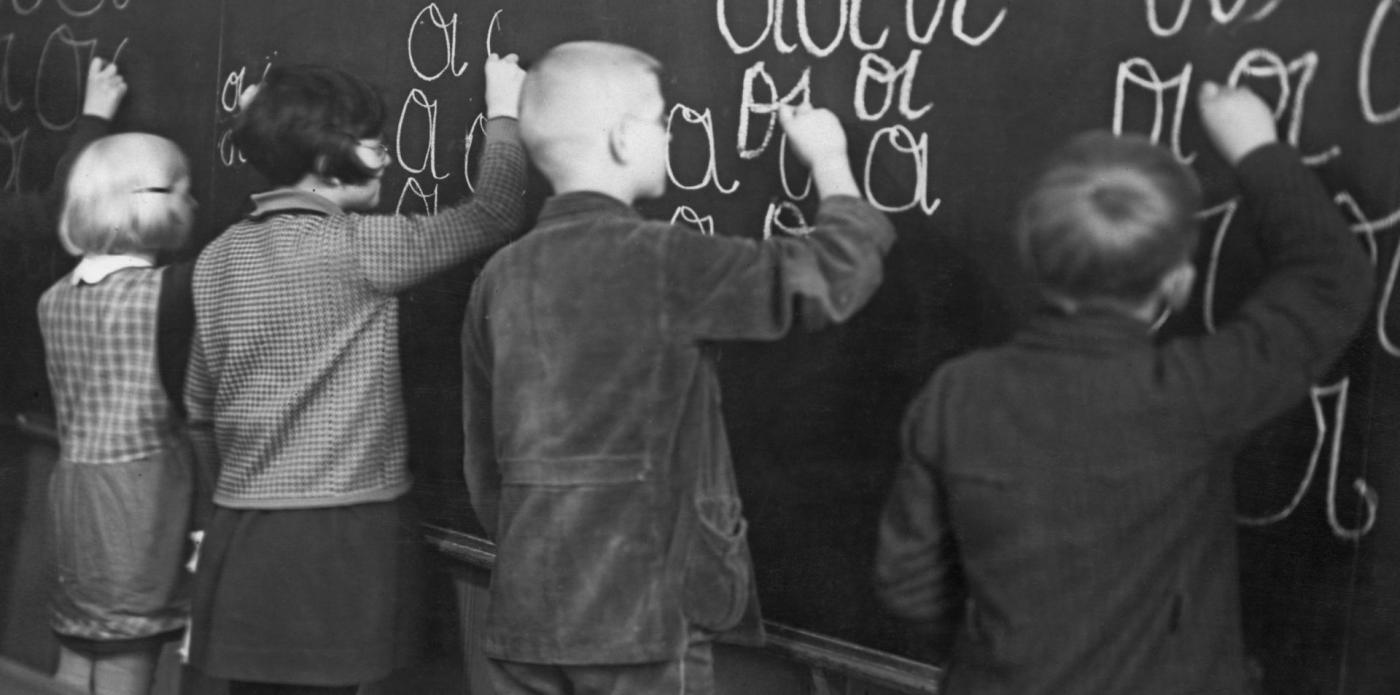 Quattro bambini si esercitano contemporaneamente alla lavagna nella scrittura di alcune lettere dell'alfabeto