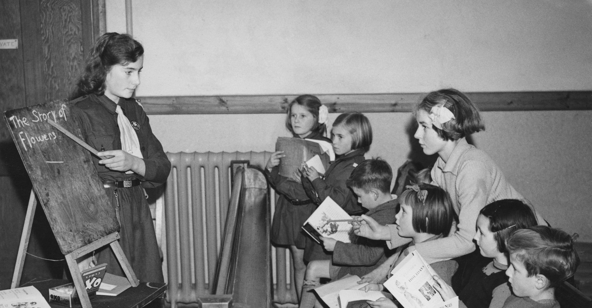 Un'adolescente indica qualcosa alla lavagna a un gruppo di bambine e bambini seduti in un'aula