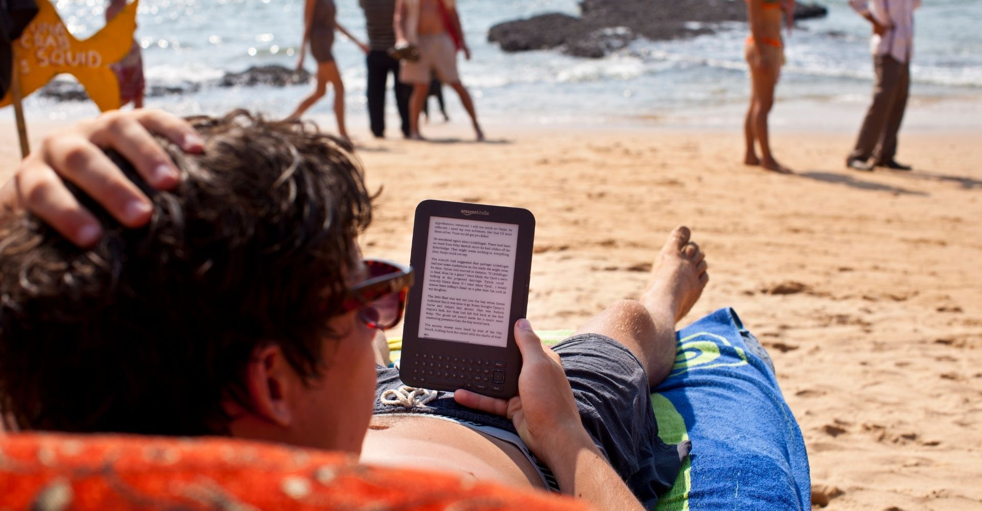 Un ragazzo legge da un e-reader mentre e sdraiato su una spiaggia