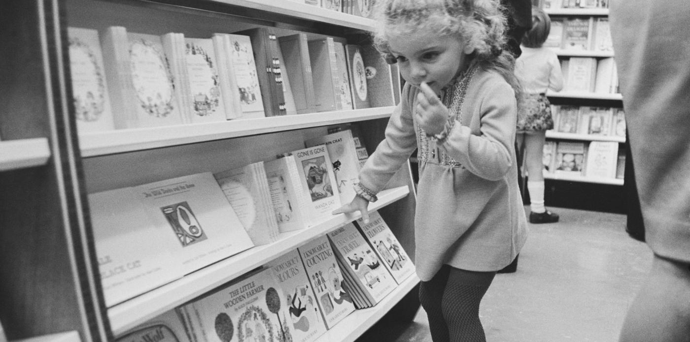 Una bambina dentro una libreria guarda i libri di alcuni scaffali