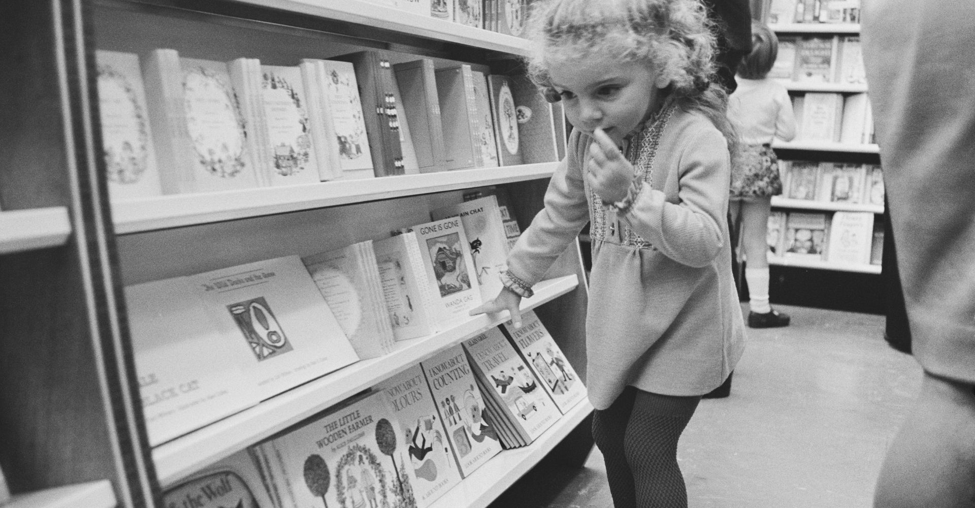 Una bambina dentro una libreria guarda i libri di alcuni scaffali