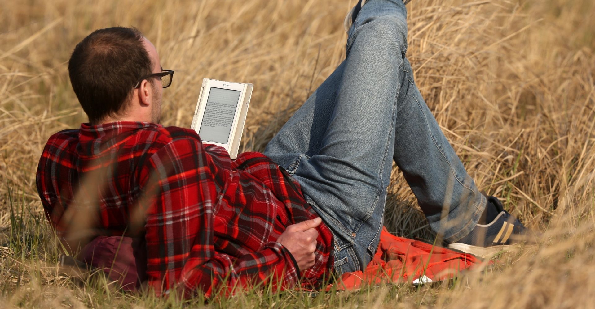 Un ragazzo di spalle legge da un e-reader mentre è sdraiato su un prato