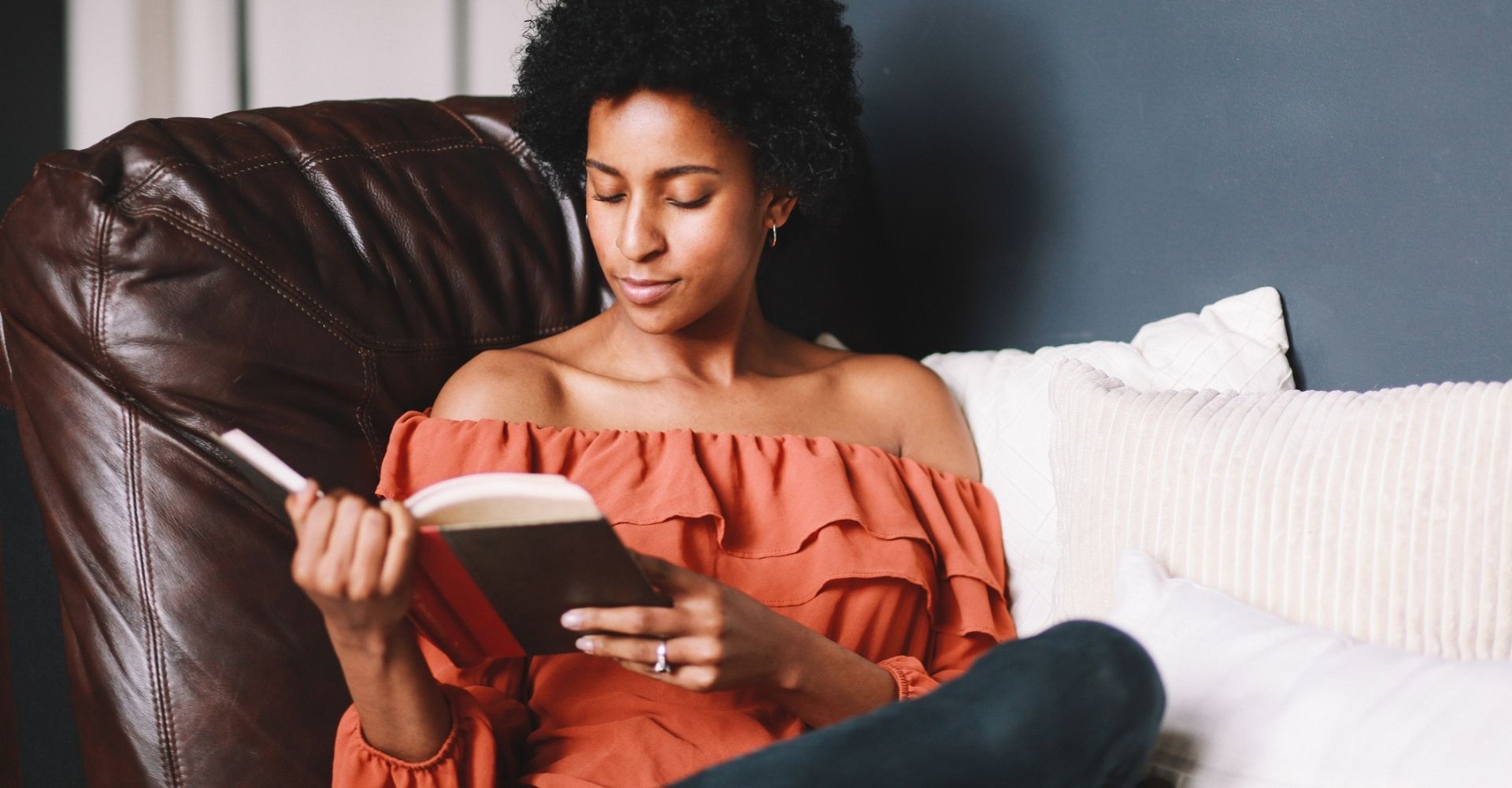 Giovane donna afroamericana legge un libro seduta su un divano