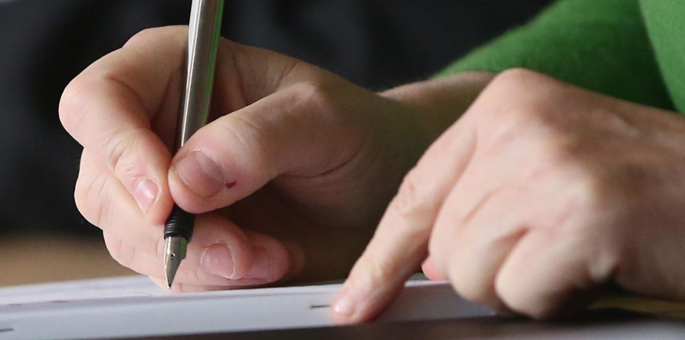 Primo piano di due mani, la destra scrive con una penna stilografica su un foglio di carta