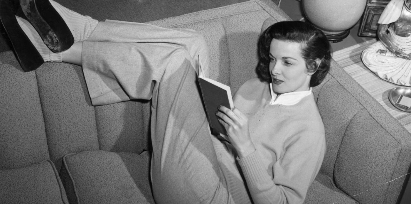 Jane Russell legge un libro sdraiata su un divano