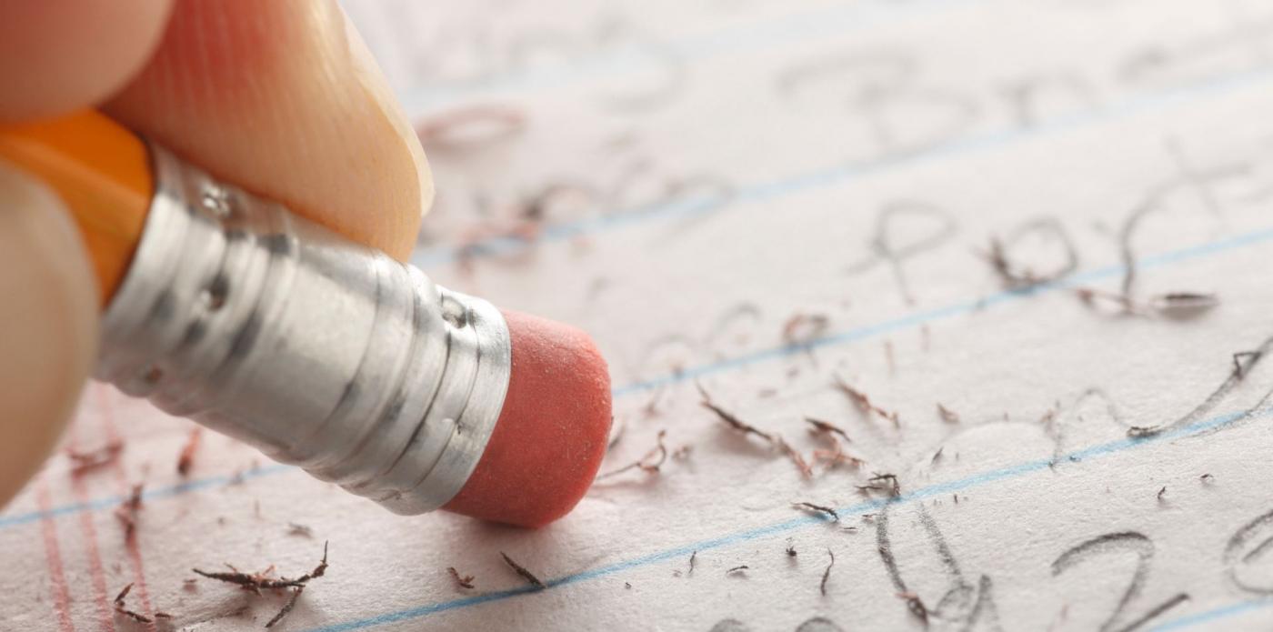 Una mano cancella con la gomma di una matita alcune scritte su un foglio di carta