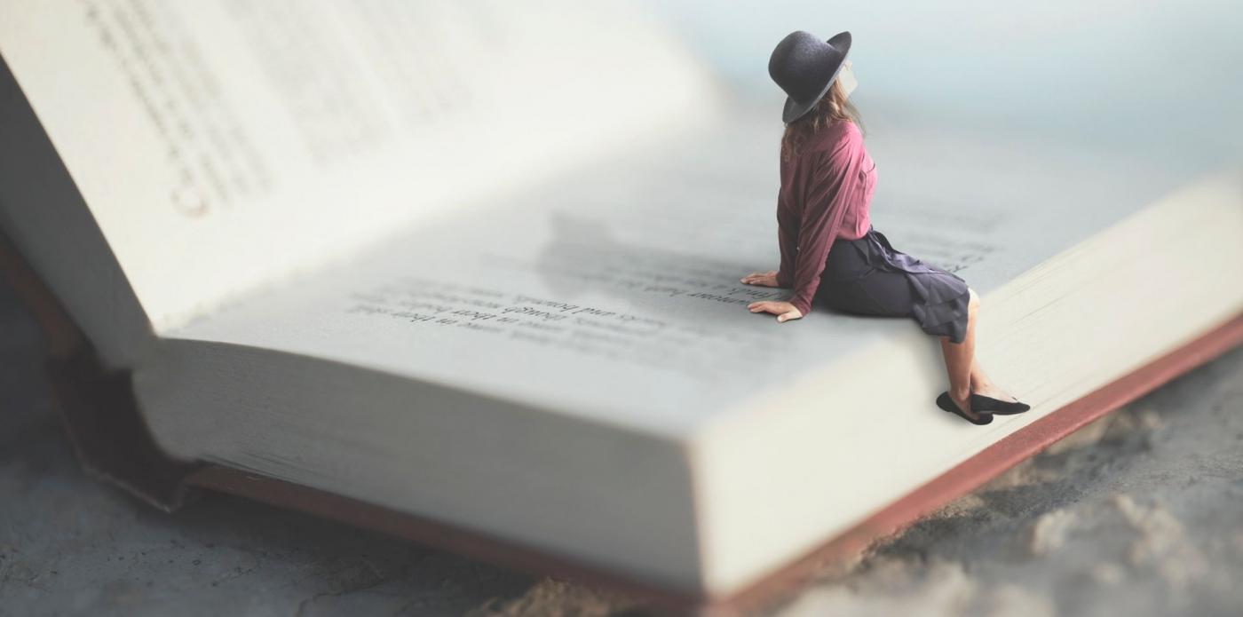 Una ragazza guarda verso l'alto seduta su un libro aperto gigante