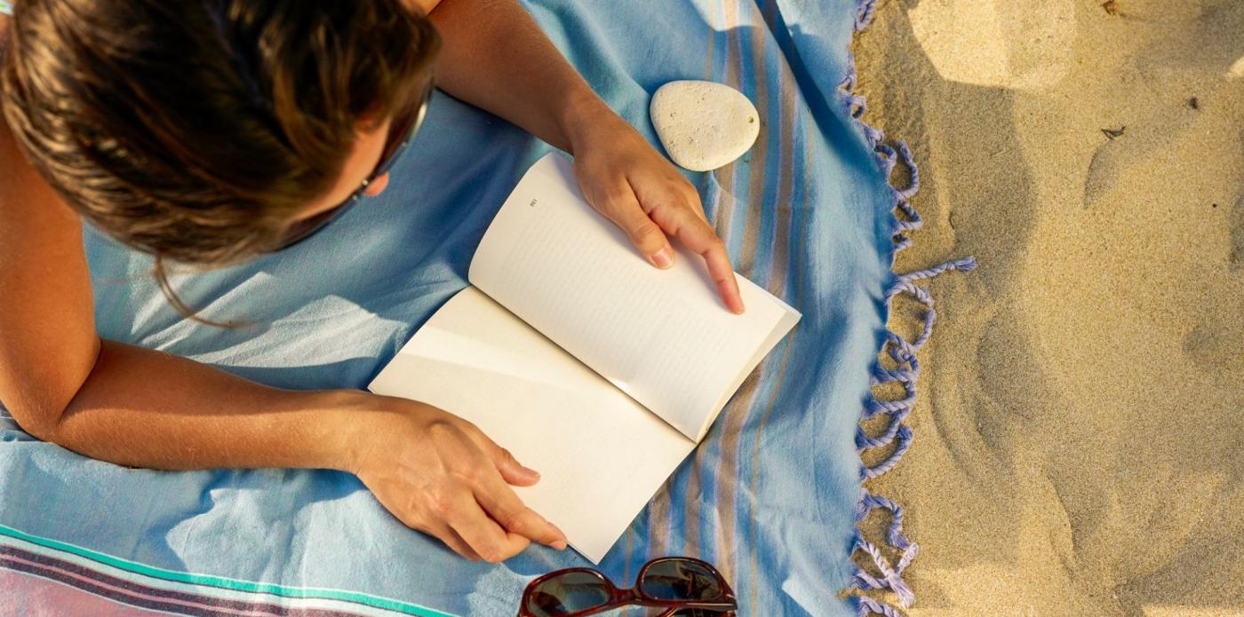 Vista aerea di una donna che legge un libro sdraiata su un telo da mare in spiaggia