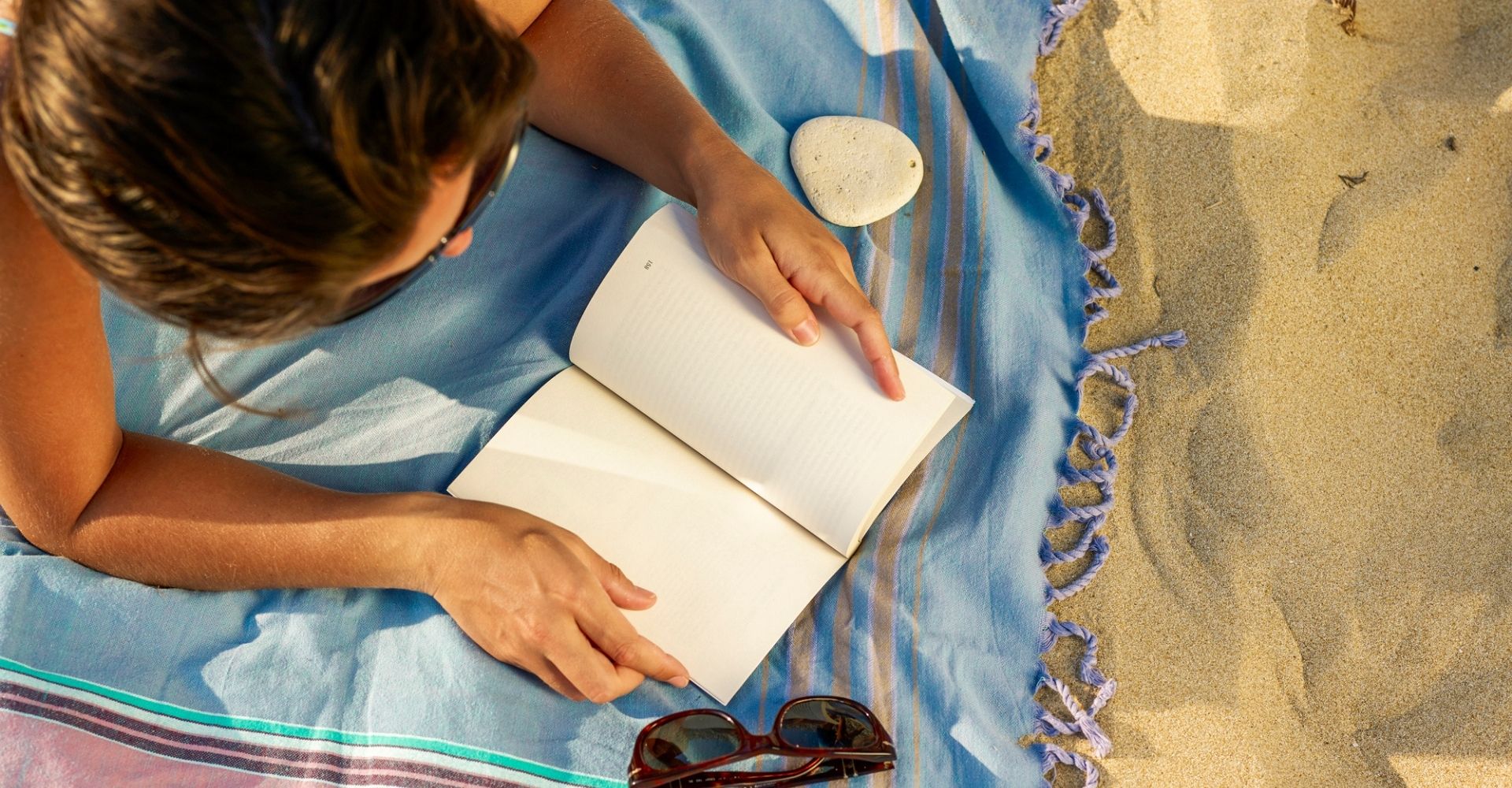 Vista aerea di una donna che legge un libro sdraiata su un telo da mare in spiaggia