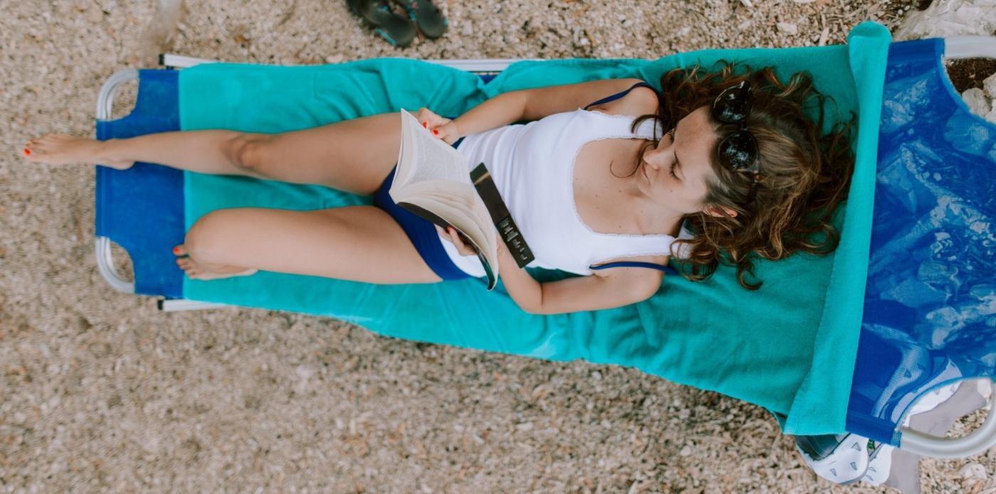 Veduta aerea di una ragazza che legge un libro su un telo da mare d'estate su una spiaggia