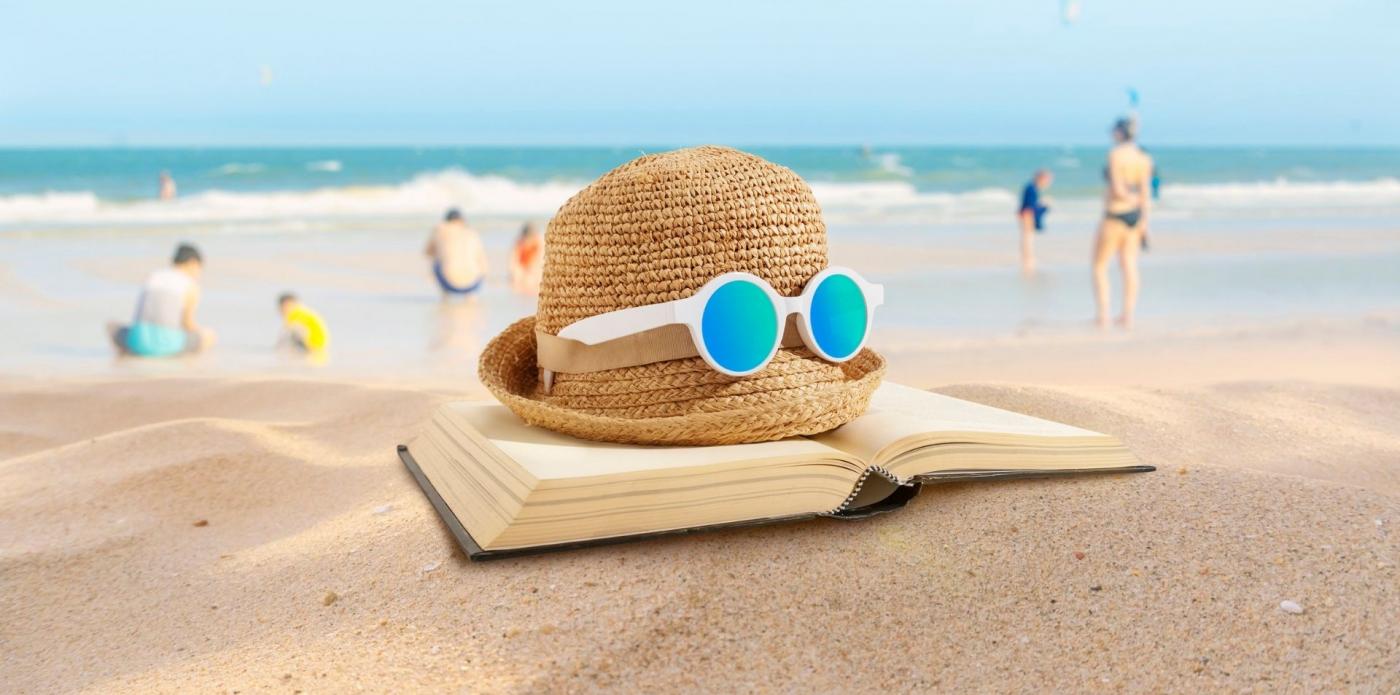 Una composizione composta da un libro aperto, un cappello di paglia e un paio di occhiali da sole su una spiaggia