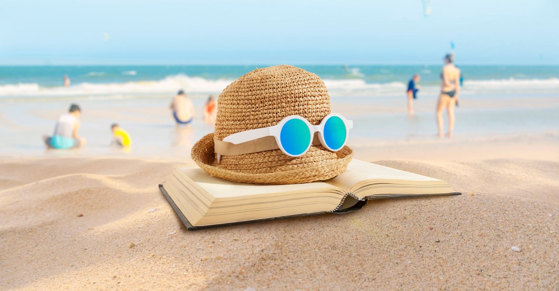 Una composizione composta da un libro aperto, un cappello di paglia e un paio di occhiali da sole su una spiaggia