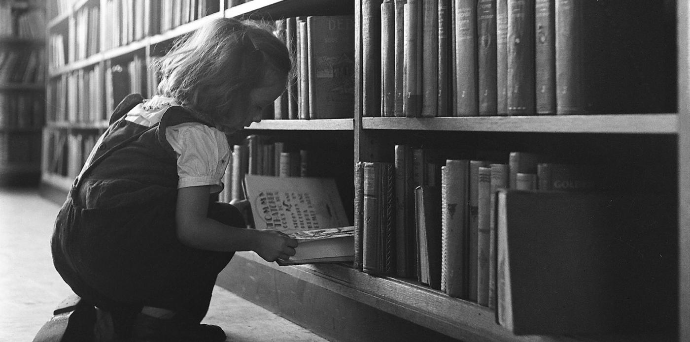 Una bambina seduto per terra in una libreria tiene fra le mani un libro