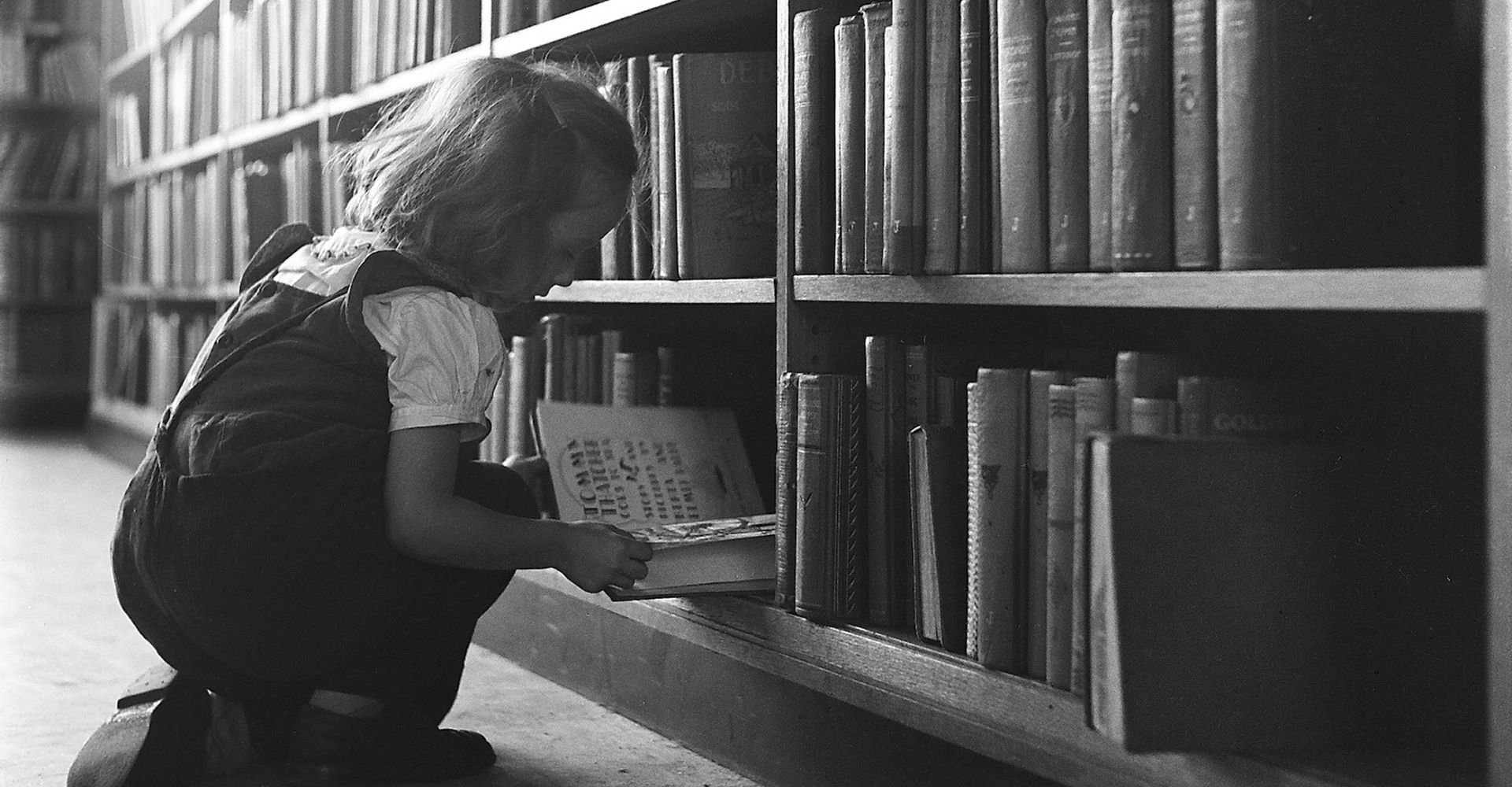 Una bambina seduto per terra in una libreria tiene fra le mani un libro