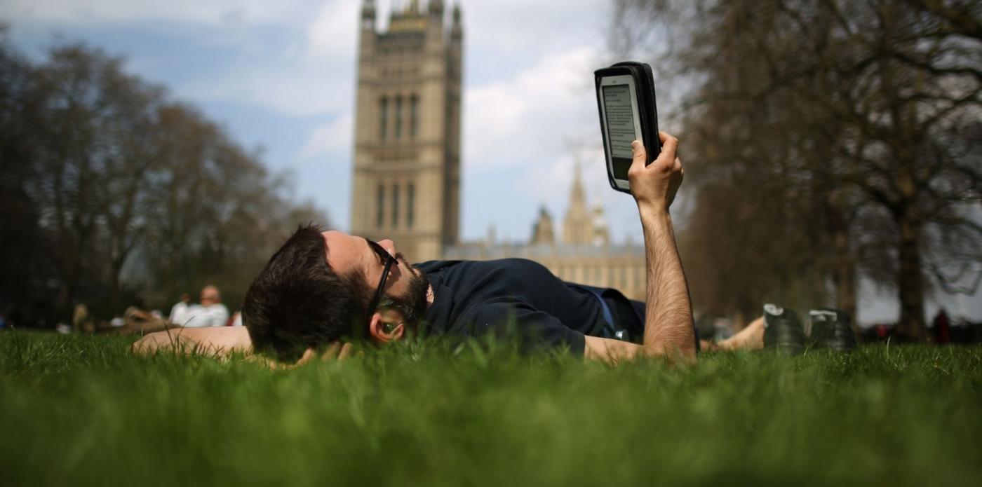 Un ragazzo sdraiato su un prato a Londra legge un libro da un ebook reader