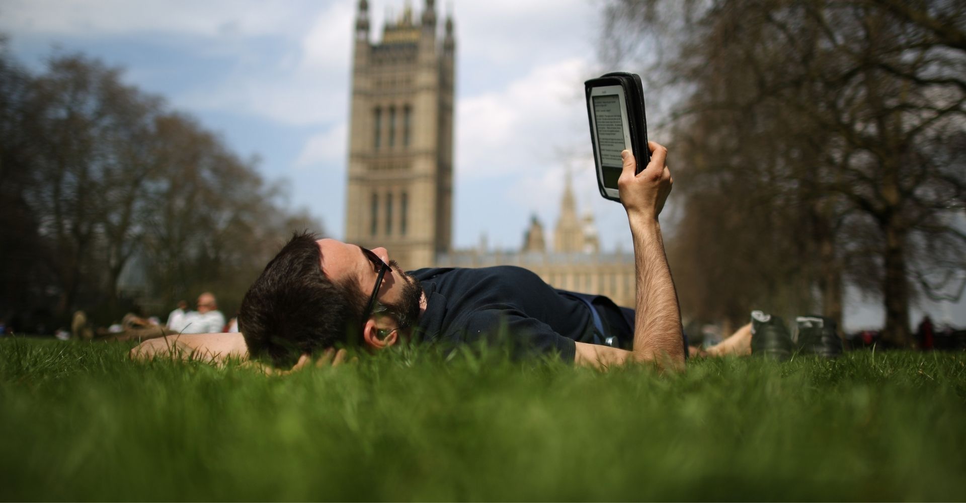 Un ragazzo sdraiato su un prato a Londra legge un libro da un ebook reader