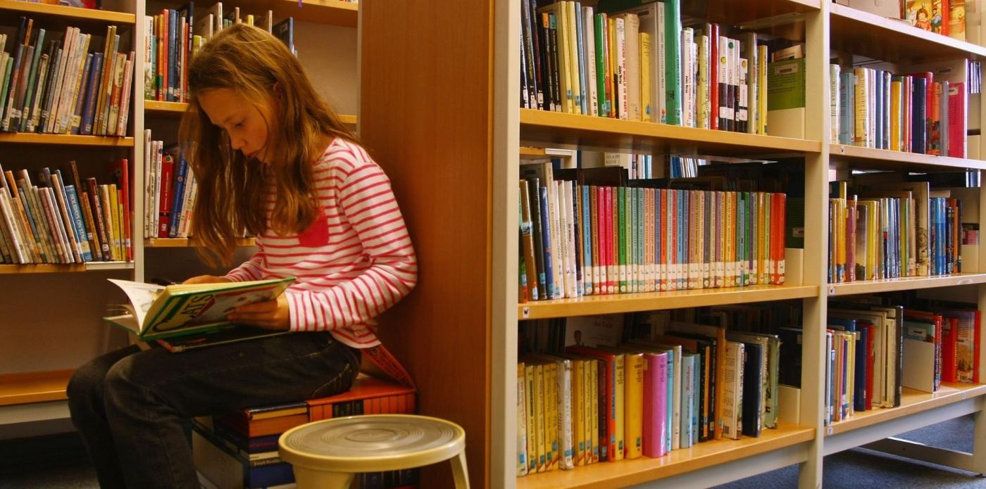 Una ragazzina legge un libro seduta su uno sgabello in una libreria