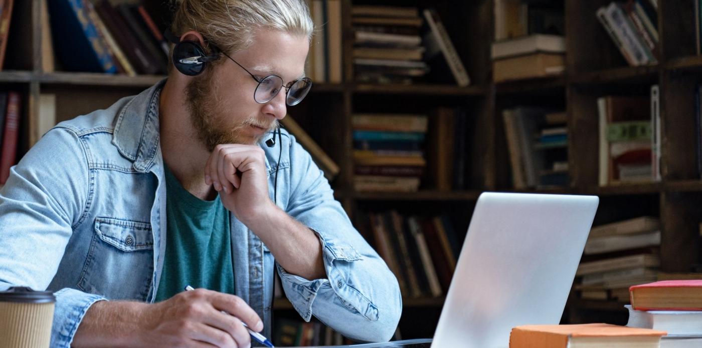 Ragazzo che ascolta un podcast o audiolibro davanti a un computer in biblioteca