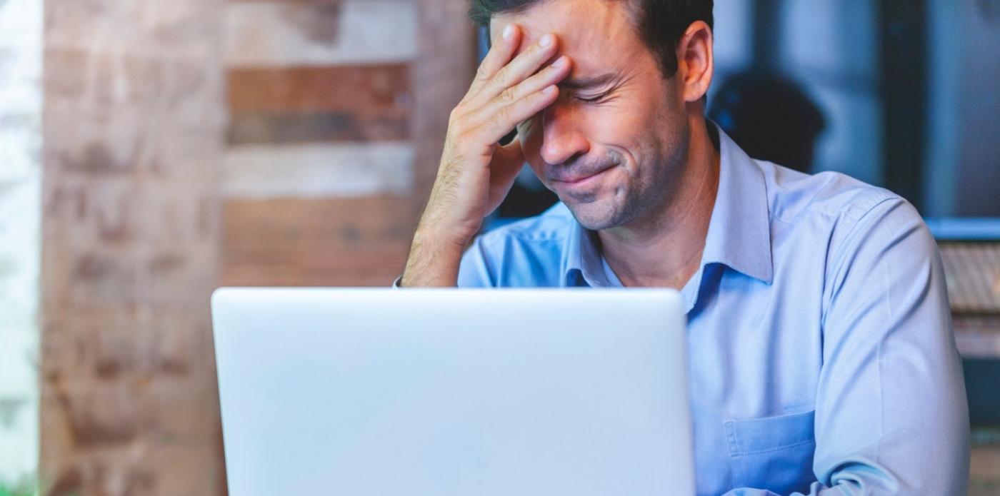 Un uomo seduto davanti al pc si passa una mano davanti agli occhi