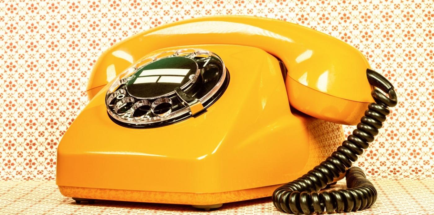 Un telefono retrò giallo su una parate e con dietro una carta da parati vintage