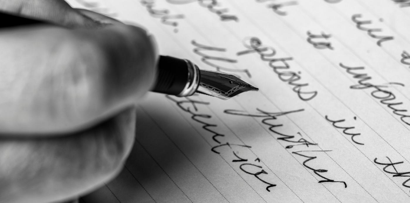 Dettaglio di una mano che scrive con una penna stilografica su un foglio di carta