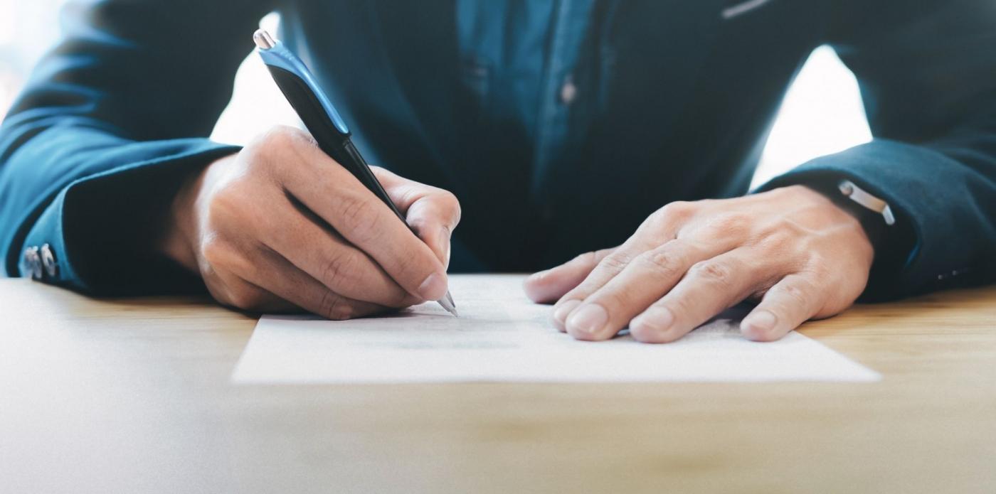 Un uomo che scrive appoggiato su un tavolo