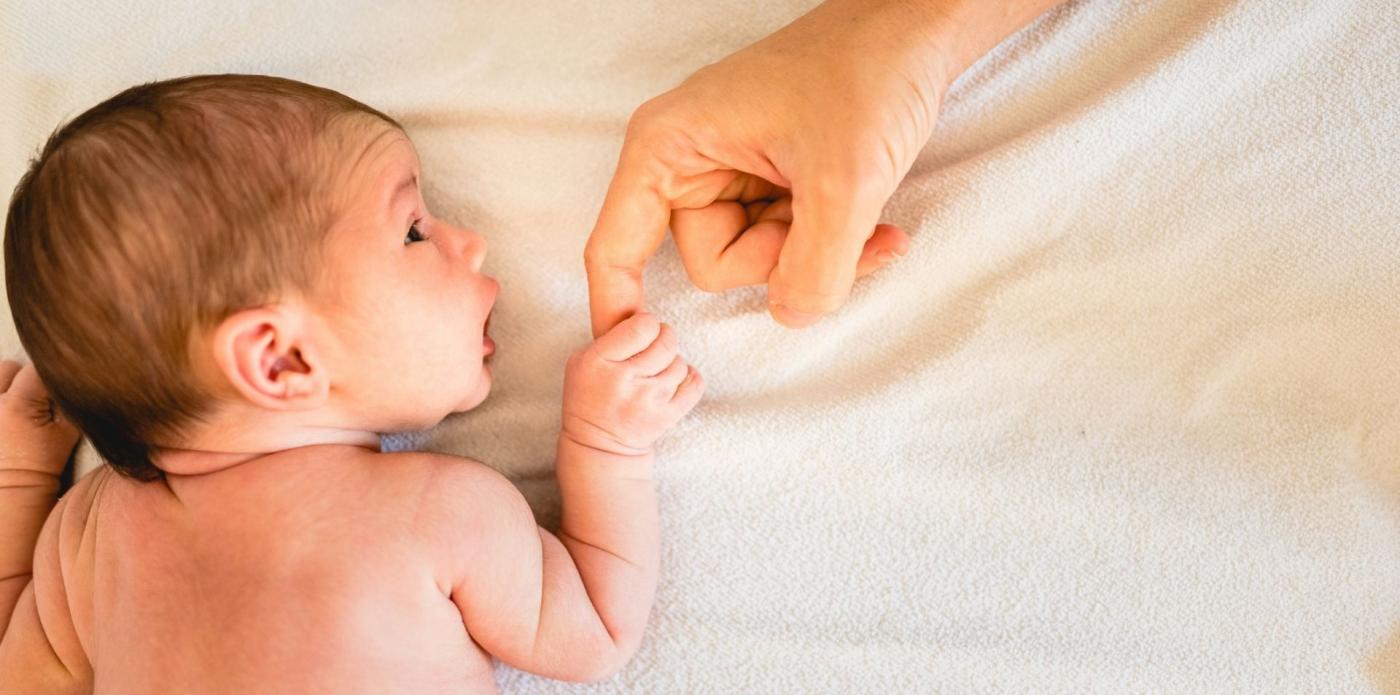 Un neonato sdraiato stringe il dito di un adulto