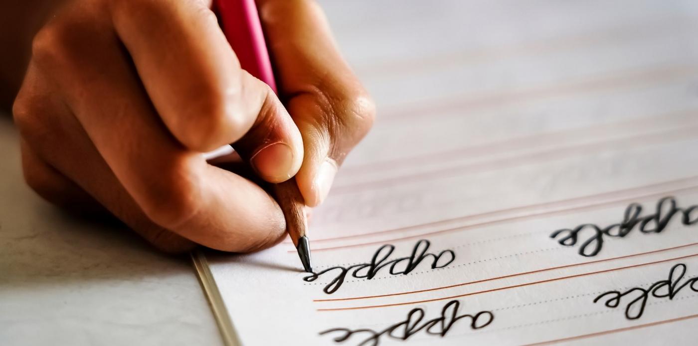 Primo piano della mano di un bambino che scrive con una matita delle parole su un foglio di carta