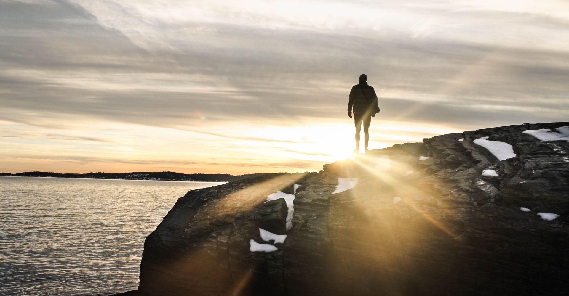 Un uomo su un dirupo guarda verso il sole all'orizzonte