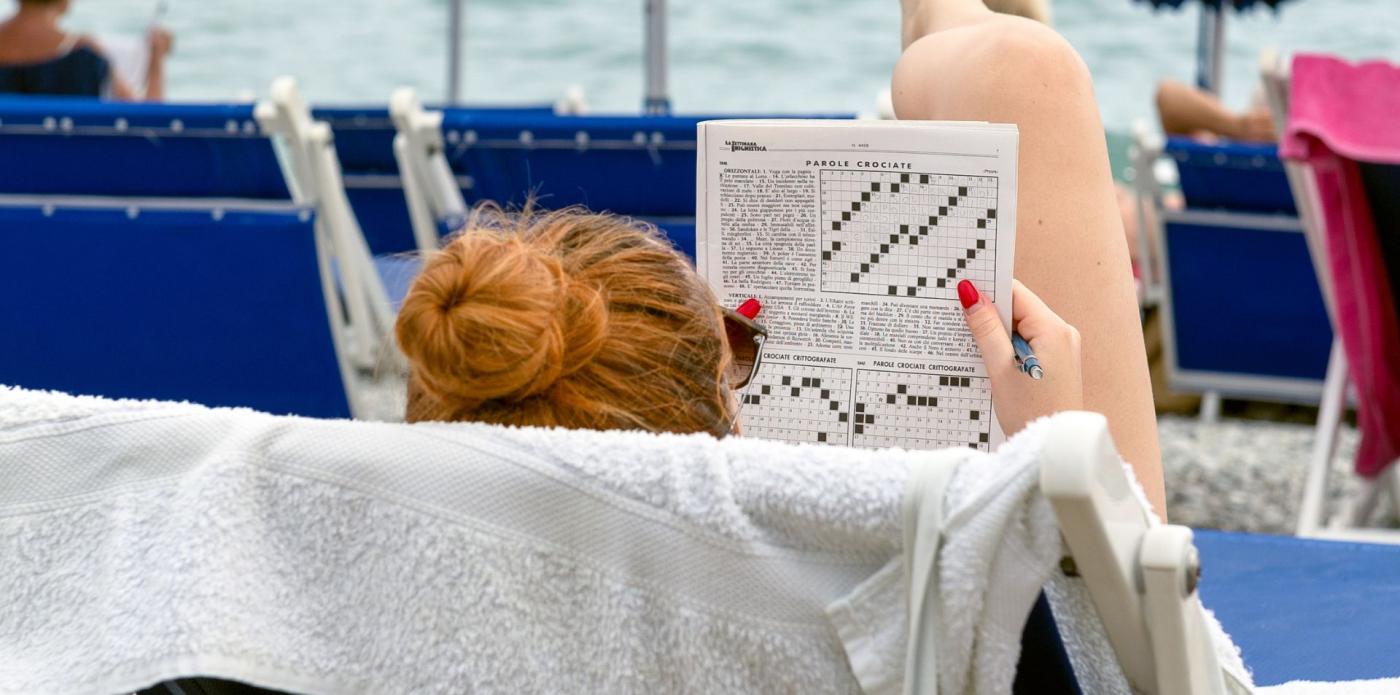 Una donna di spalle fa un cruciverba sulla spiaggia d'estate