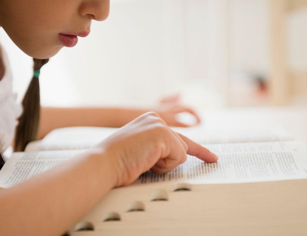 Primo piano di una studentessa che consulta di profilo un dizionario mentre è seduta al banco