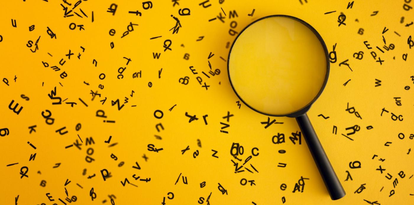 Una lente di ingrandimento circondata di lettere sparpagliate su un piano giallo