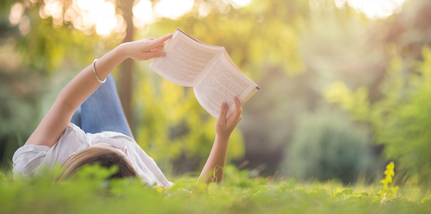 una ragazza legge un libro sdraiata sul prato