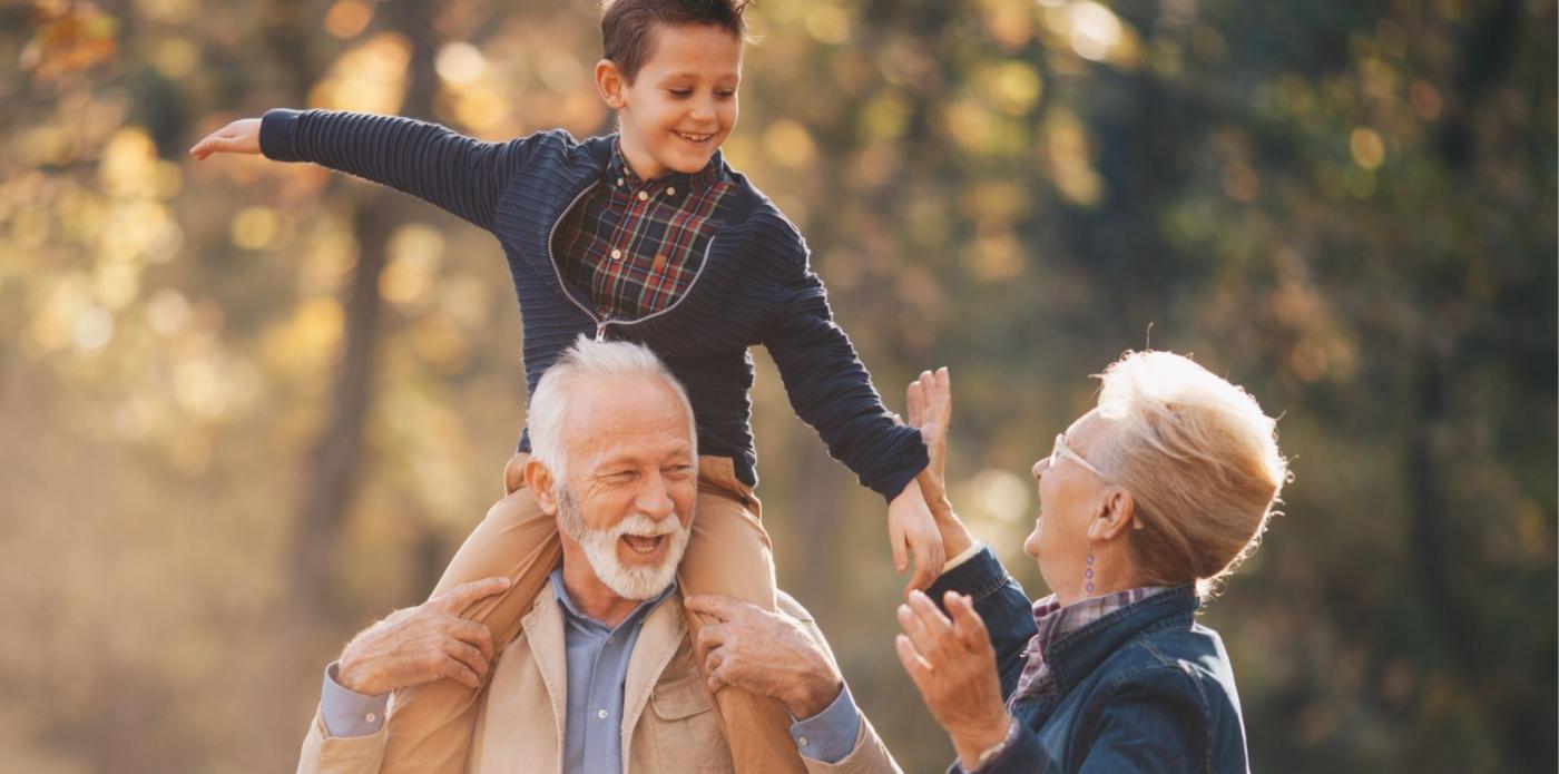 Un bambino sorride mentre sta seduto sulle spalle del nonno e in compagnia della nonna in un parco