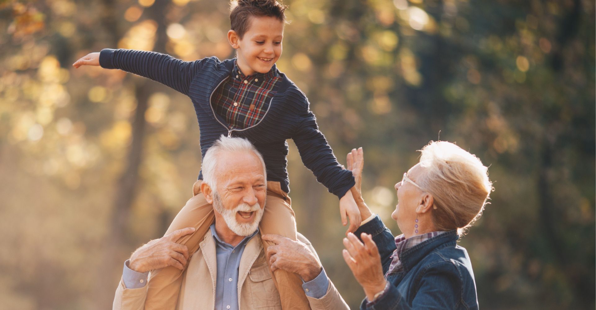 Un bambino sorride mentre sta seduto sulle spalle del nonno e in compagnia della nonna in un parco