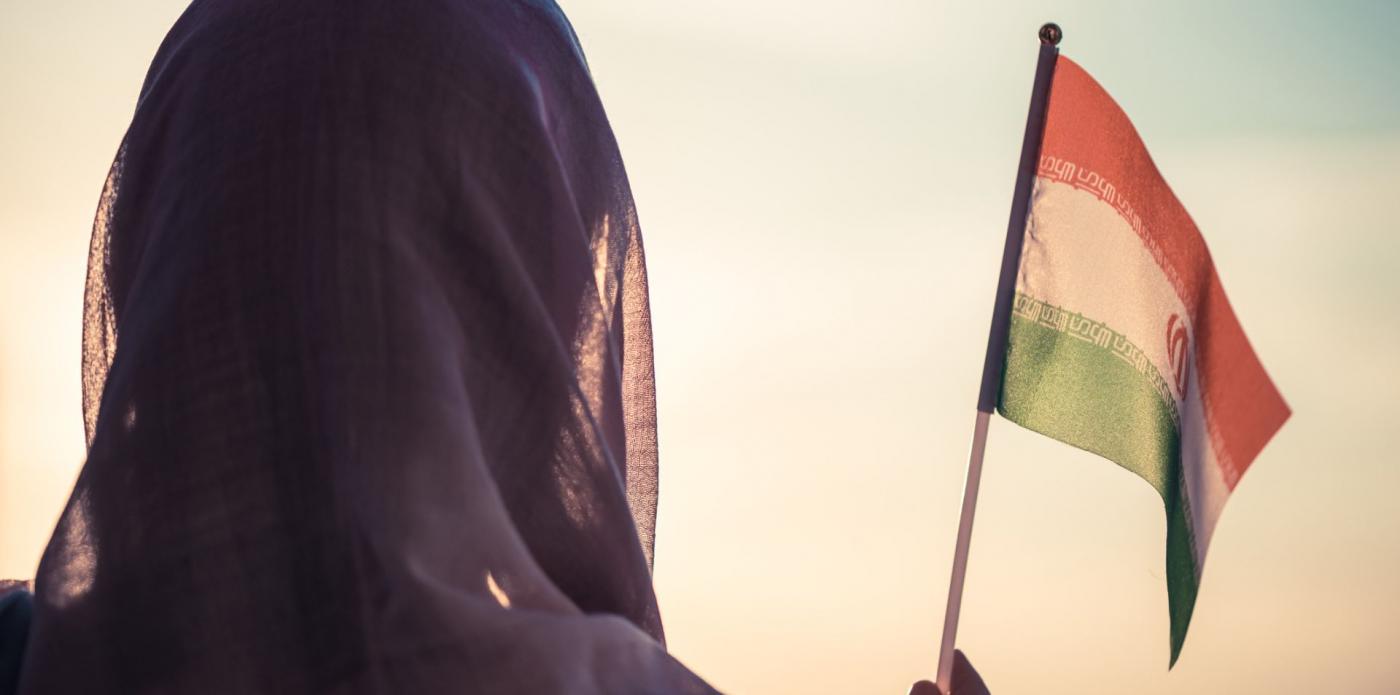 Una donna di spalle che indossa il velo agita una bandiera dell'Iran