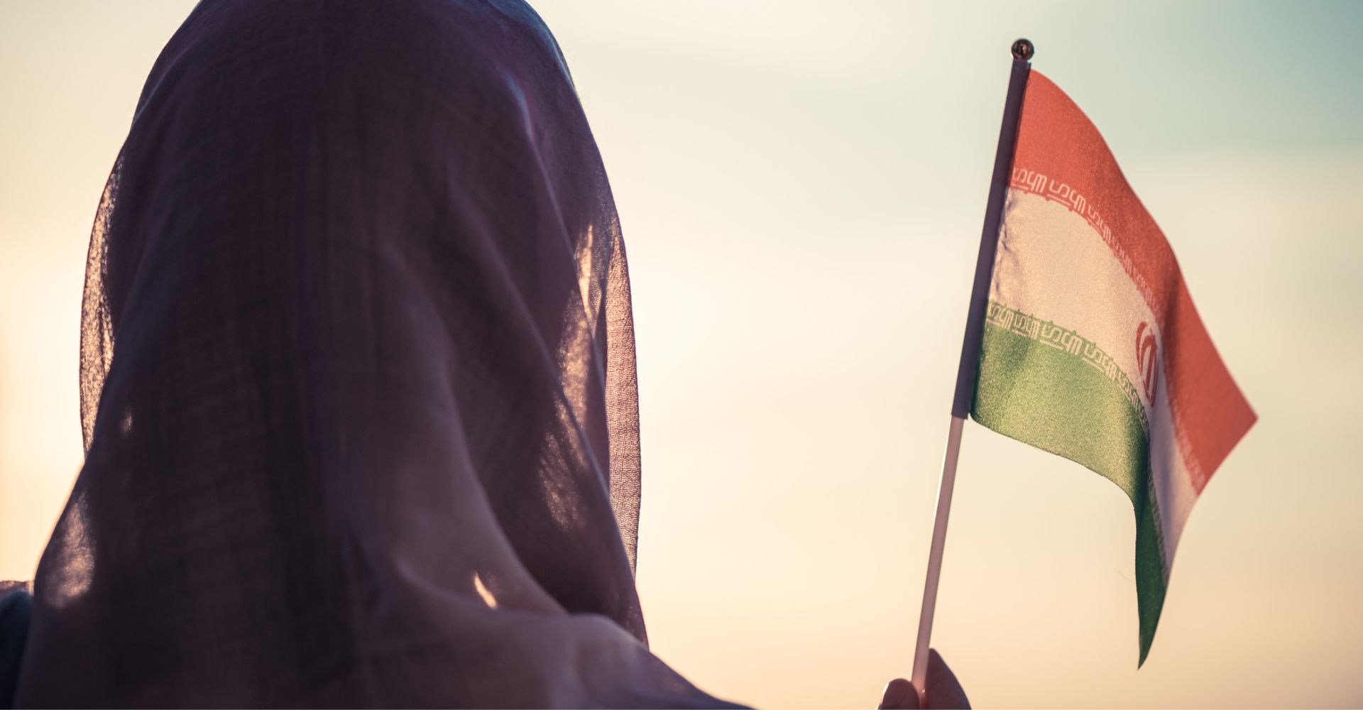 Una donna di spalle che indossa il velo agita una bandiera dell'Iran