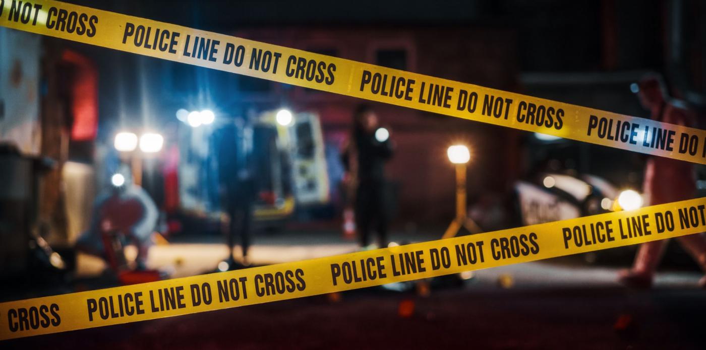 Scena del crimine notturna, con una squadra investigativa sullo sfondo che lavora su un omicidio