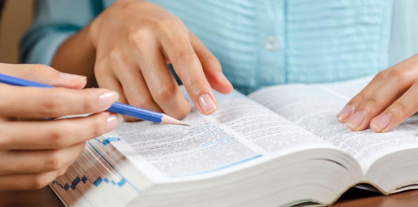 Primo piano di un vocabolario consultato da una ragazza e da una persona accanto a lei che tiene in mano una matita